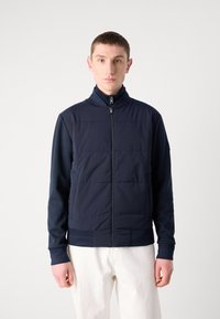 Navy blue jacket featuring a zippered front, padded torso, and contrasting long sleeves. Soft texture with ribbed cuffs and hem.