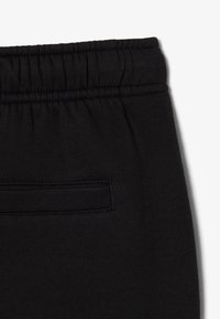 Zwarte stoffen broek met elastische tailleband en een enkele horizontale paspelzak aan de achterkant.