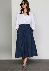 Denim maxi seelik, millel on ühtlane vöökoht ja vööga disain, plekkide ja sääreüleste äärtega. Kombineeritud valge nööpidega särk.