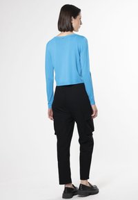 Blauer, verkürzter Pullover mit langen Ärmeln, der über einen rechteckigen Ausschnitt und ein kleines Detail am Rücken verfügt, kombiniert mit schwarzen Cargo-Hosen und klobigen Schuhen.