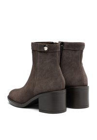 Brown suede ankle boots with a round toe, mid-height block heel, and a zip closure. Features a button accent on the cuff.