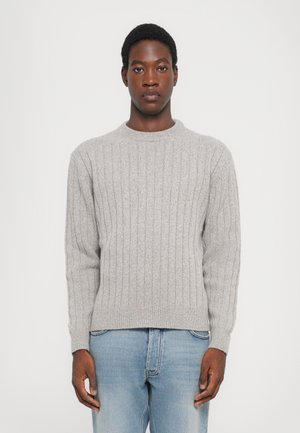 Grau gerippter Strickpullover mit Rundhalsausschnitt, strukturiertem Material und langen Ärmeln, kombiniert mit hellblauen Jeans.