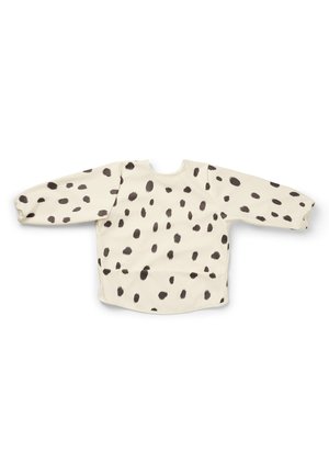 Langærmet beige småbørnsforklæde med sorte uregelmæssige pletter, elastiske manchetter og en afrundet halsudskæring, lagt fladt mod en hvid baggrund.