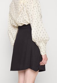 Saia preta em forma de A com uma textura suave, combinada com uma blusa creme com padrão floral e mangas pregueadas em forma de puff.