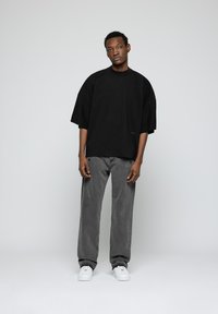 Camiseta negra de gran tamaño con mangas cortas, combinada con jeans rectos grises y zapatillas blancas. Diseño simple y sin adornos, con un ajuste relajado.