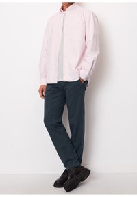 Chemise à rayures rose clair avec poche, associée à un pantalon bleu marine et des chaussures à lacets noires, présentée sur un fond blanc.
