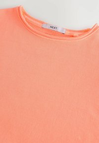 Peachfarvet T-shirt lavet af blødt, struktureret stof med rund halsudskæring og et "NEXT" mærke i midten på bagsiden.
