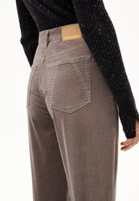 Brown corduroy pants with vertical ribbing, featuring two back pockets and a tan leather brand label at the waistband.
