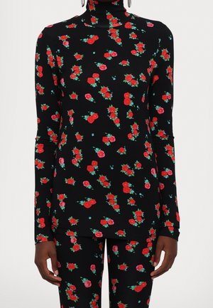 Zwarte coltrui en broek met rood en roze bloemenprint gedragen door persoon met een middeldonkere huidskleur en oorringen.
