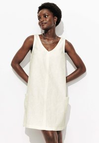 Robe blanche sans manches à décolleté en V, avec un motif texturé, dotée de deux poches latérales et d'une coupe décontractée. Ourlet court.