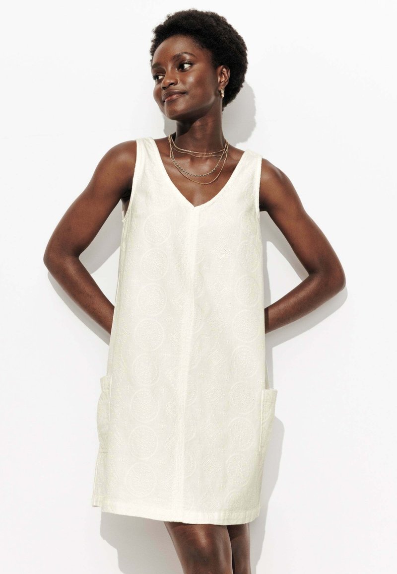 Robe blanche sans manches à décolleté en V, avec un motif texturé, dotée de deux poches latérales et d'une coupe décontractée. Ourlet court.