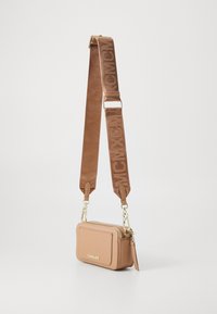 Borsa a tracolla compatta di colore beige con zip dorata, tasca frontale e ampia tracolla regolabile con branding tono su tono.