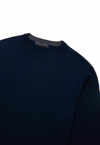 Tmavě modrý svetr s kulatým výstřihem, texturovanou tkaninou a žebrovaným límečkem. Obsahuje štítek se zlatým písmem na výstřihu.