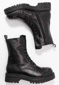 Czarne skórzane buty wojskowe z wiązaniem z przodu, zamkiem błyskawicznym po boku, dekoracyjnymi metalowymi detalami na czubku oraz gumową podeszwą z bieżnikiem.