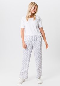 Witte top met korte mouwen en patroon op de schouders, gecombineerd met lichtgrijze loungebroeken met een patroon en een ovale vorm, en witte sneakers.