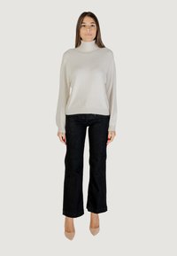 Un pull col roulé gris clair à coupe décontractée, associé à un jean noir à jambe droite et des escarpins beiges. Le pull a un subtil éclat.