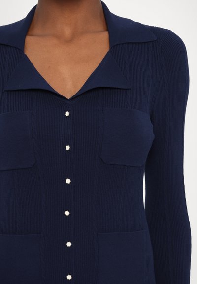 Cardigan a maglia navy con colletto, caratterizzato da una texture a coste, due tasche sul petto e bottoni decorativi in colore a contrasto.