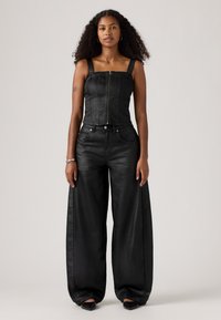 Combinaison en denim noir avec un corsage ajusté, un décolleté carré et des pantalons à jambes larges. Dotée d'une fermeture éclair frontale, de grandes poches et d'une texture lisse.