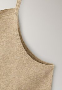 Débardeur en tricot beige avec fines bretelles et encolure arrondie sur un fond gris clair.