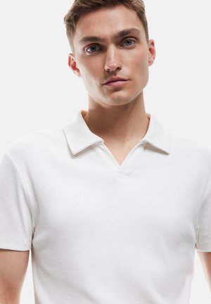 Camisa polo blanca de canalé con escote en V corto y cuello doblado, que presenta una silueta ajustada y una textura suave.