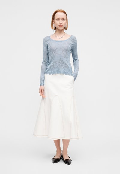 Pull en maille côtelée bleu clair avec motif floral, associé à une jupe trapèze blanche avec coutures apparentes. Ballerines noires pointues.