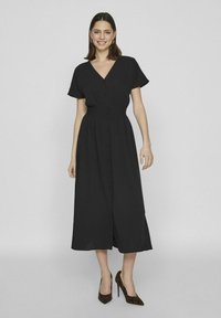 Čierne šaty strednej dĺžky s krátkymi rukávmi, výstrihom do V a zapínaním na gombíky. Ľahký materiál s zúženým pásom a splývavou sukňou. Topánky s leopardím vzorom.