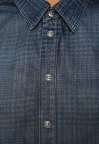 Πουκάμισο από τζιν με σκούρο μπλε καρό μοτίβο, κουμπωμένο μέχρι το γιακά, με ασημένια κουμπιά με λογότυπο και ομαλή υφή.