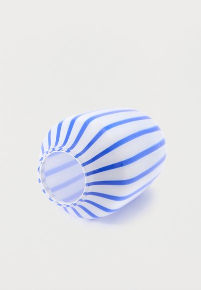 Λευκό γυάλινο βάζο με κάθετες μπλε ρίγες, που βρίσκεται πλαγιασμένο σε ένα απλό φωτεινό φόντο.