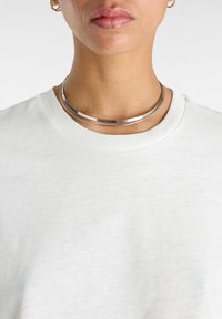 Söljmetal halsband med två släta, runda band i nära skikt. Bärs över en ljusgrå t-shirt med rundad hals och en subtil textur.