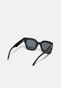 Ochelari de soare negri cu un design geometric, lentile gri, și montură neagră lucioasă. Caracteristici hardware aurii pe laterale și accente multicolore.