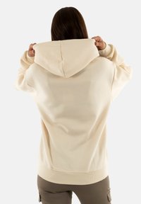 Sudadera con capucha crema de corte relajado, con puños y dobladillo acanalados; tela suave; sin patrones visibles ni detalles metálicos.