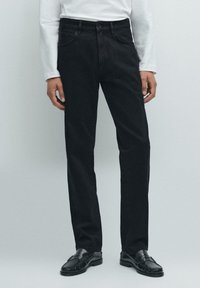 Jeans in denim nero con design a gamba dritta, dotati di chiusura con bottone, passanti per cintura e cinque tasche. Indossati con mocassini neri.