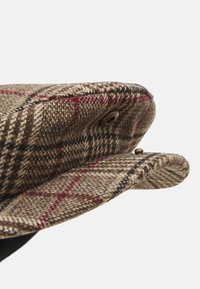 Gorra de cuadros marrón hecha de lana con una superficie texturizada. Presenta un borde redondeado, forro negro y un ojal de metal para ventilación.
