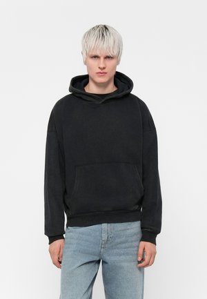 Black hoodie with a front pocket, relaxed fit, and ribbed cuffs. Paired with light blue denim jeans. Minimalist design, no visible patterns.