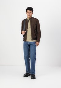 Brun suedebomberjakke med ståkrave, parret med en lys T-shirt og blå denimjeans. Sorte sko fuldender looket.
