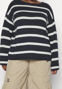 Maglione a righe navy e bianche con scollatura ampia e maniche lunghe, abbinato a pantaloni cargo beige chiaro con tasche.