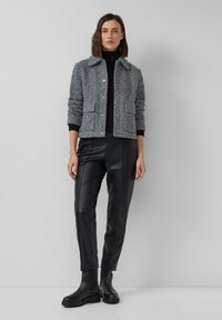 Giacca grigia con texture, colletto, due tasche frontali, chiusura a bottoni, abbinata a pantaloni in pelle nera e stivali neri alla caviglia.