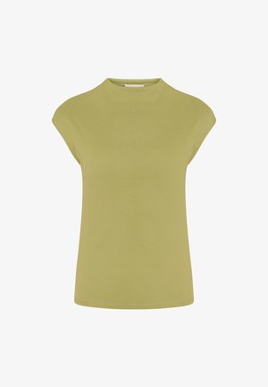 Femme aux cheveux lisses et foncés portant un haut sans manches vert olive, un pantalon large vert clair et des sandales à talons noires sur un fond uni.