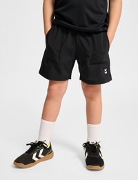 Svarta sportshorts med sidfickor, tillverkade av lättv�ävt material. Kombinerade med svarta skor med vita detaljer och ljusgröna inslag.