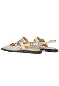Flat sandalen in crèmekleurig leer met een puntige neus, voorzien van meerdere banden en een decoratief metalen detail. Zwarte rubberen zool.