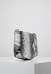 Kleine Tasche mit Schuppenmuster in Schwarz und Weiß, mit strukturiertem Design, glatter Textur und metallischen Akzenten am Reißverschluss.