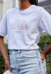 Bílý bavlněný tričko s logem "The North Face" ve světle růžové barvě, ve spojení s světle modrými džíny. Pohodlný střih, krátké rukávy.