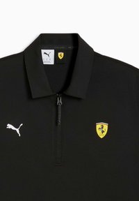 Polo noir avec fermeture éclair, arborant un logo Puma blanc et un blason Ferrari jaune, avec des accents verts et rouges. Tissu lisse et léger.