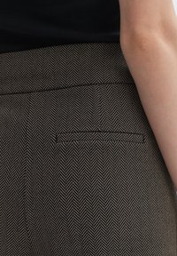 Látka s vzorem houndstooth v černé a krémové barvě, s malou zadní kapsou a hladkým pasem s jemným texturovaným detailem.