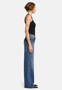 Hellblaue gerade geschnittene Jeans aus Denim mit Edelsteinverzierungen, hoher Taille und einem kontrastierenden schwarzen Oberteil, von der Seite betrachtet.