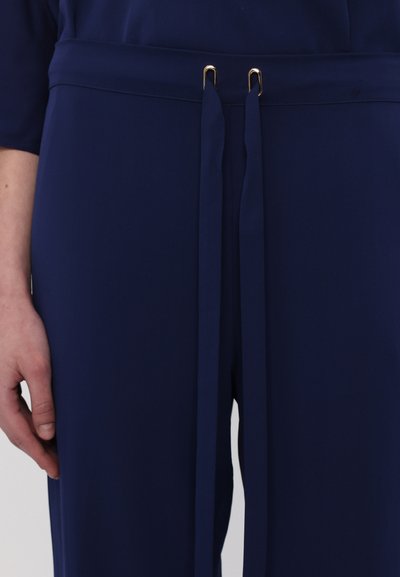Navy blue trousers with a smooth texture, featuring a wide waistband, two golden metal accents, and long fabric ties.