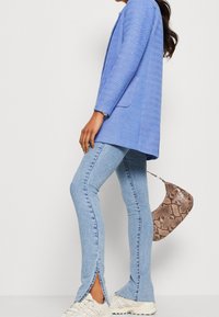 Light blue long-sleeve blazer with a herringbone texture, paired with light wash flared jeans featuring side slits. Brown snake-print handbag.