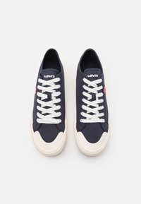 Sneakers in tela blu con lacci bianchi, punta in gomma e logo Levi's sulla linguetta. La suola è beige con una finitura texturizzata.