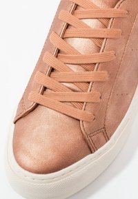 Baskets en cuir couleur or rose avec lacets plats, bout arrondi, côtés texturés et semelle en caoutchouc. Caractérisées par un design minimaliste et des détails de coutures discrètes.