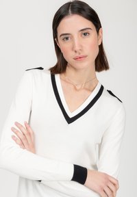 Witte en zwarte V-hals trui. Voorzien van zwarte accenten op de halslijn en manchetten, met schouderdetail. Gemaakt van zacht gebreid materiaal.